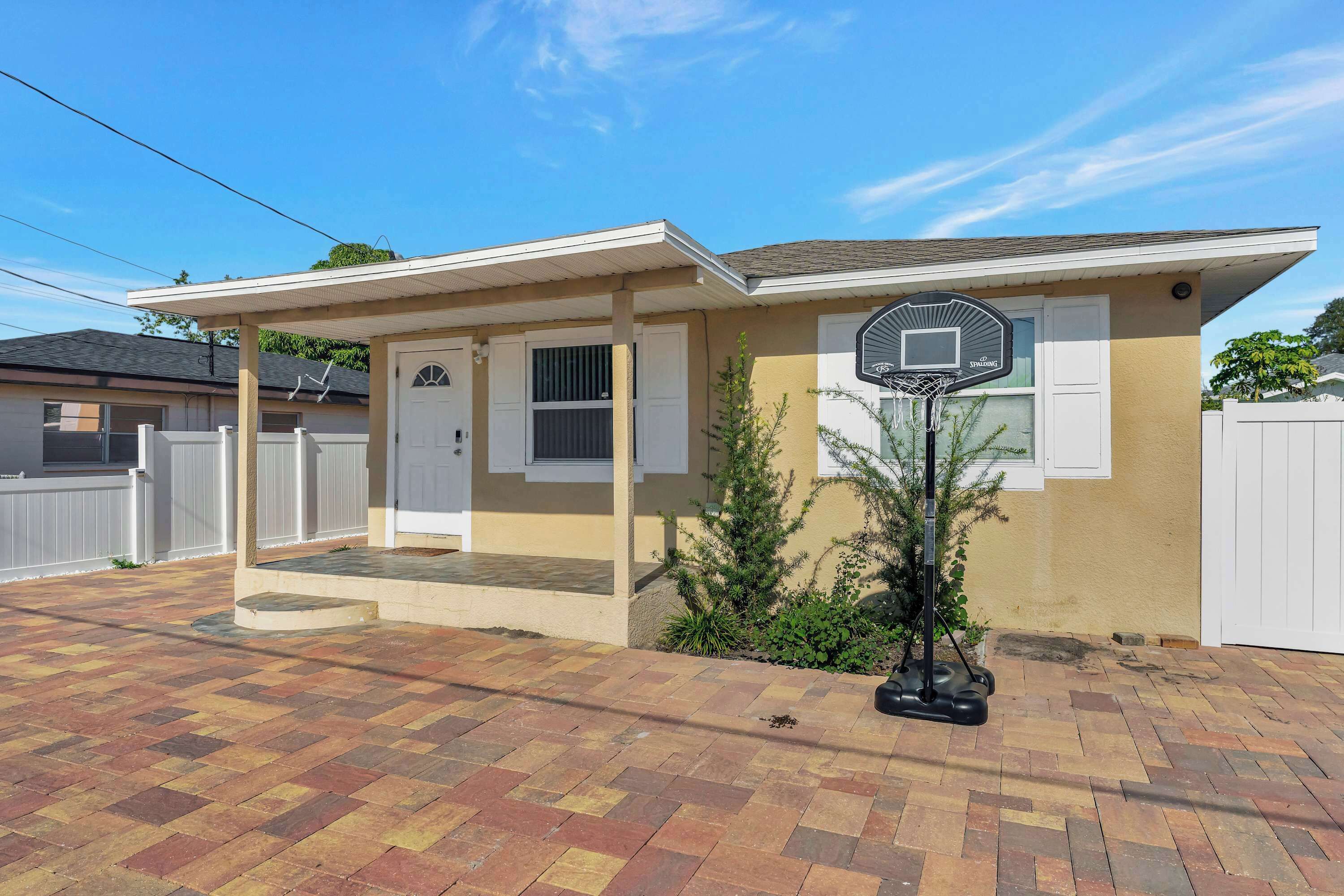 A residential house with a covered porch, a basketball hoop, and a brick driveway.