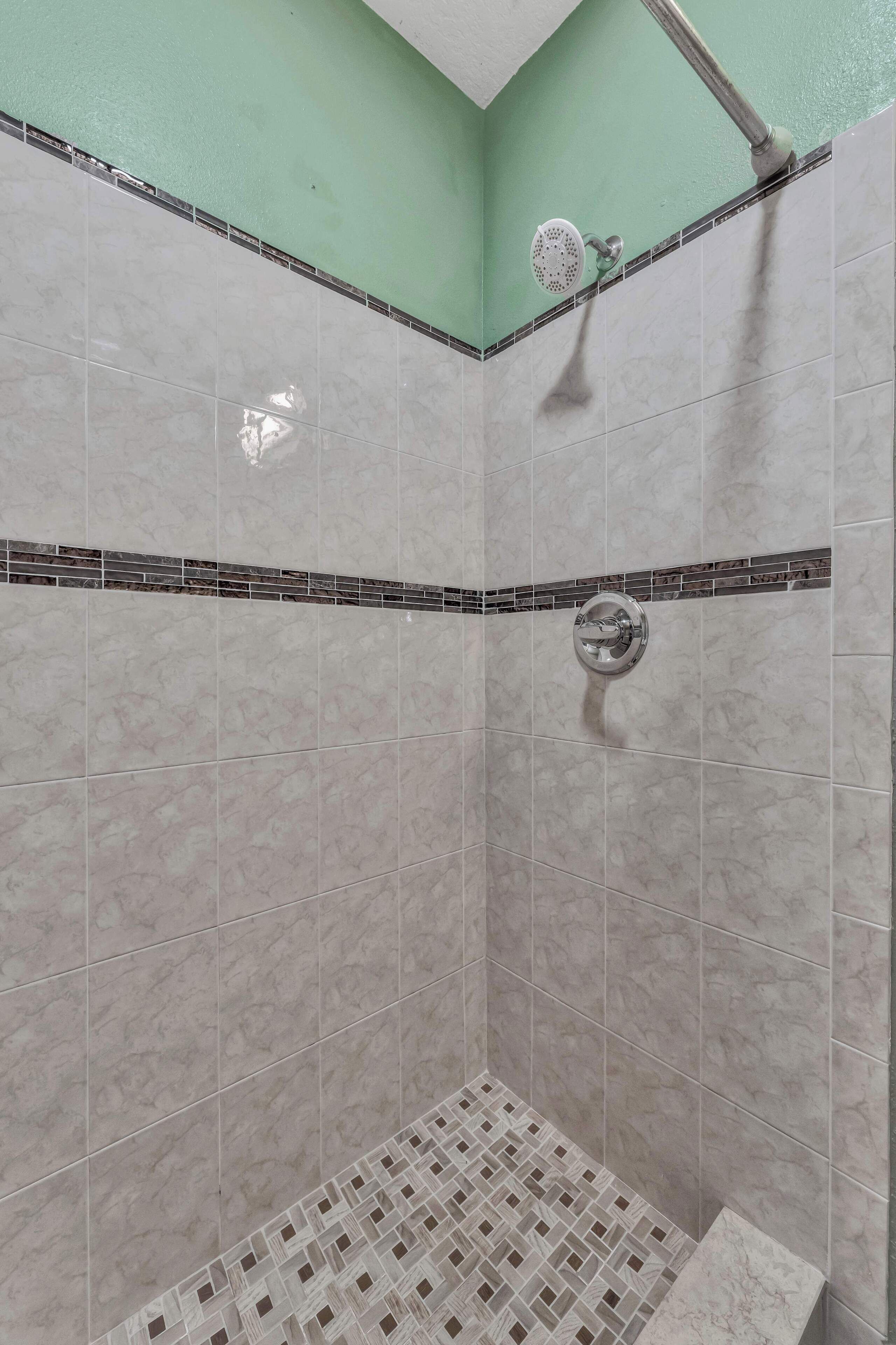 Une douche avec un mur carrelé et un pommeau de douche.