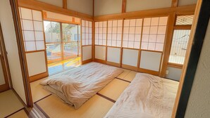 Une pièce de style japonais traditionnel, avec un sol recouvert de tatamis, un futon servant de lit, des portes coulissantes en papier de riz (shoji) et une lanterne en papier suspendue.