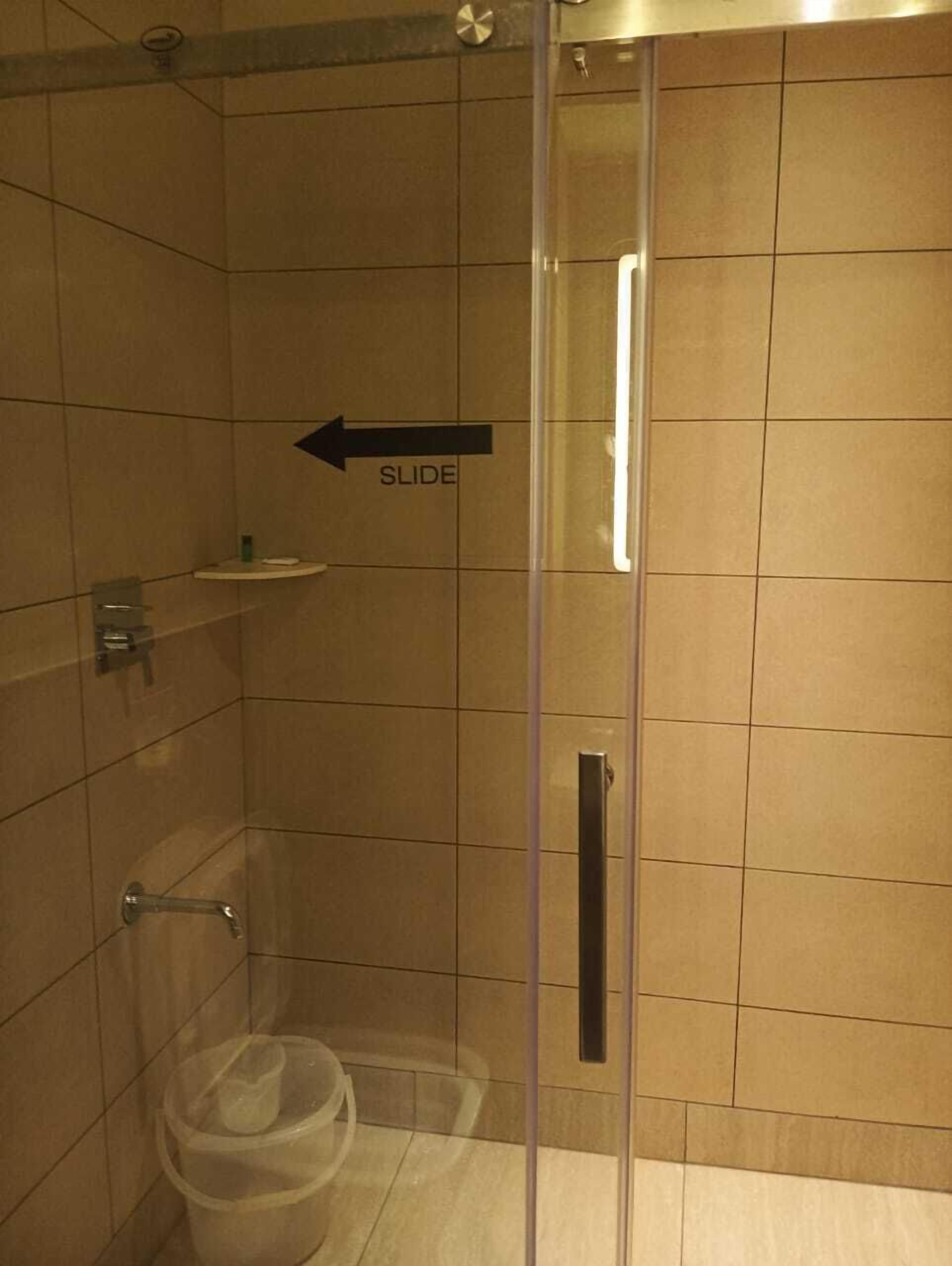 A shower area with a glass door, a sliding mechanism, and a small shelf with toiletries.
