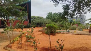 A garden area with small trees and a paved walkway. - Vanaalayam Retreat Palladam by Arcadia (Palladam)