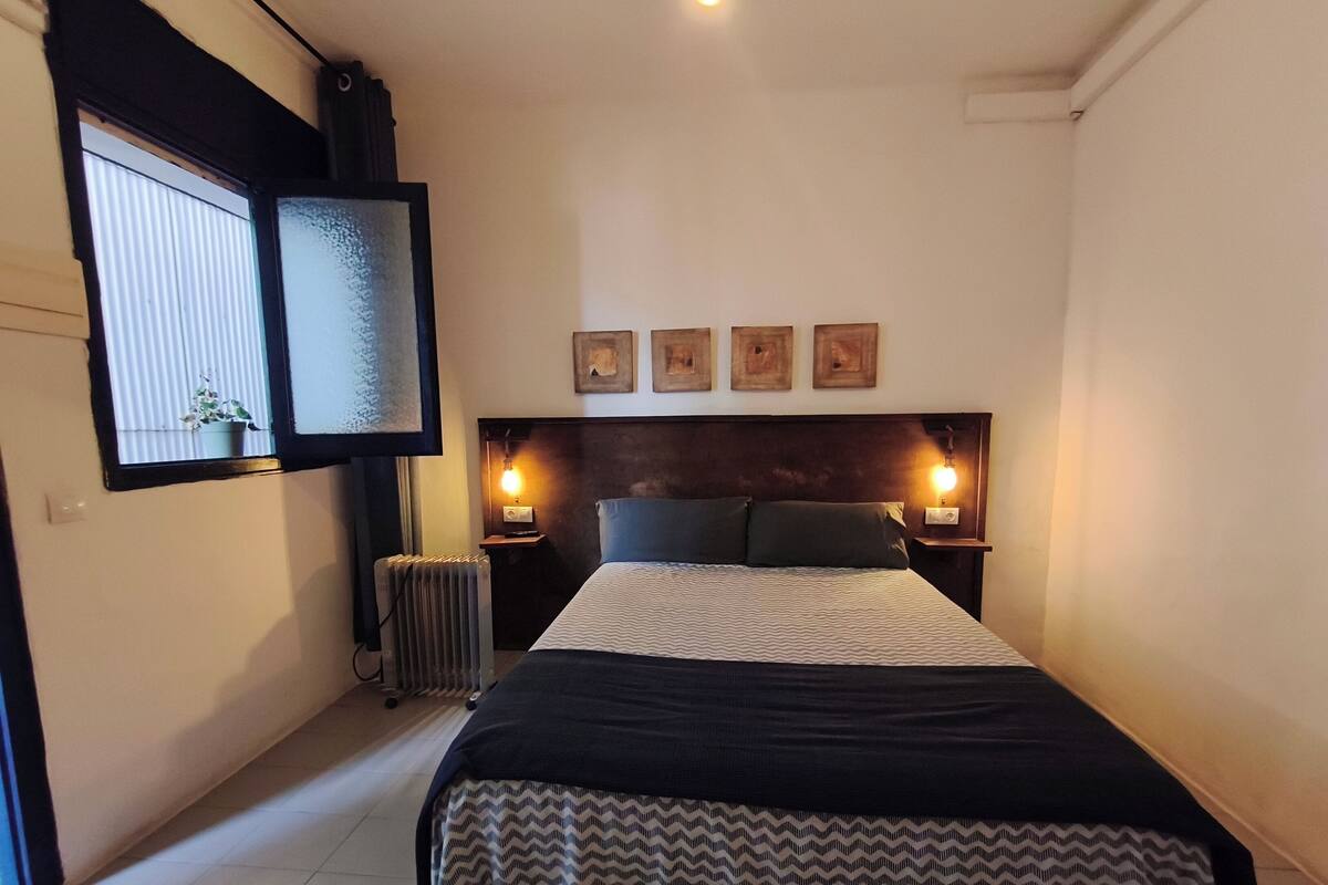 Une chambre à coucher avec un lit, deux lampes de chevet, un radiateur et une fenêtre avec des stores.