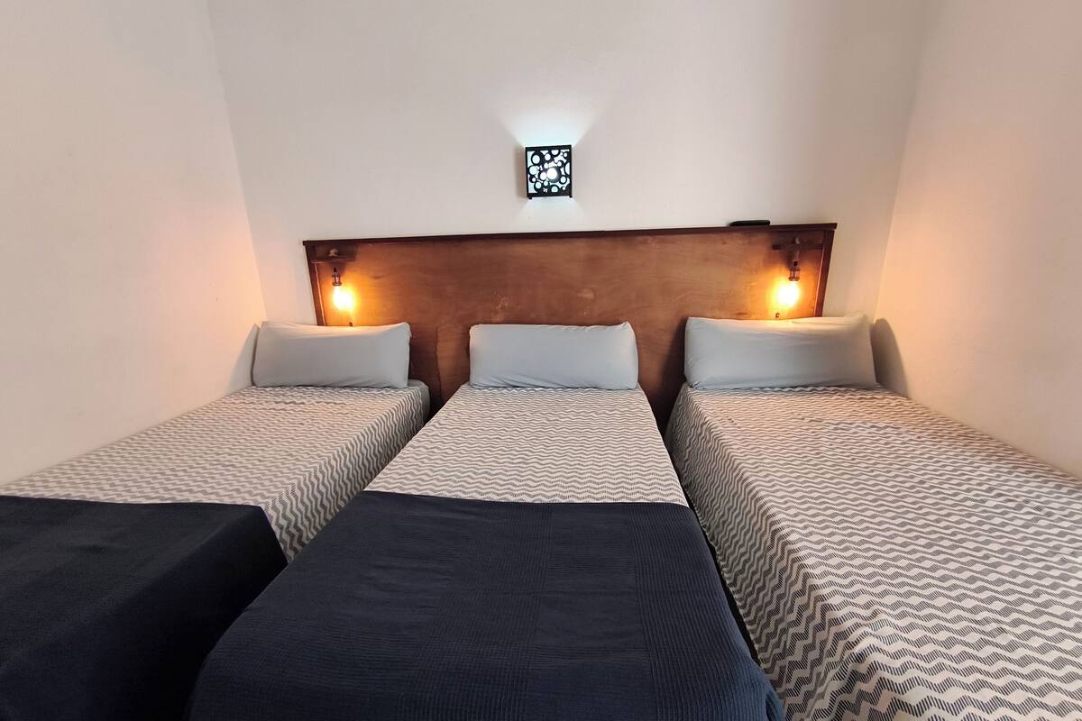Une chambre d’hôtel avec deux lits simples, chacun agrémenté d’une couvre-lit à motifs et d’un oreiller. Il y a deux tables de chevet avec des lampes, et un petit objet décoratif est accroché au mur au-dessus des lits.