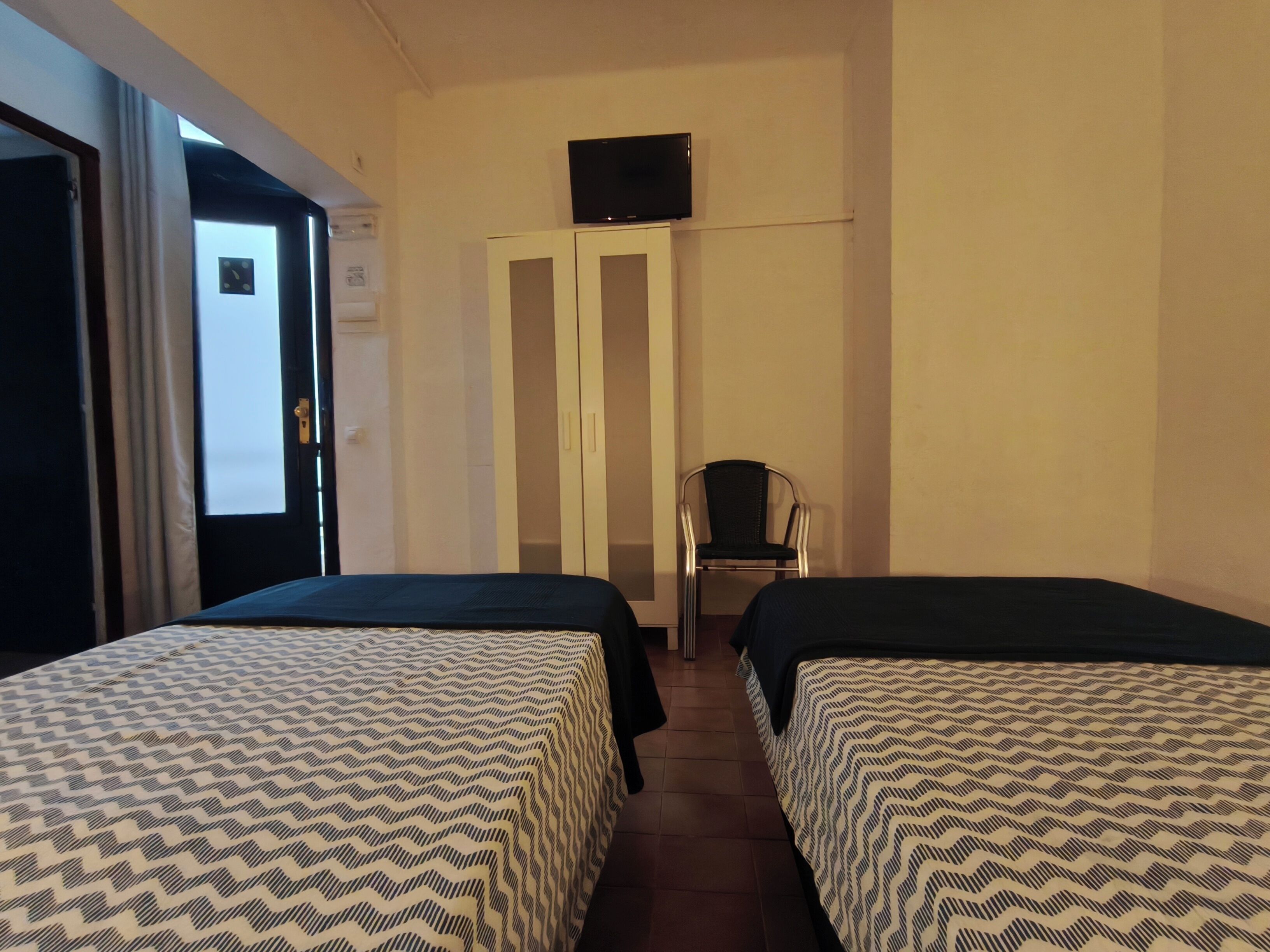 Een hotelkamer met twee bedden, een televisie aan de muur, een kledingkast en een stoel.