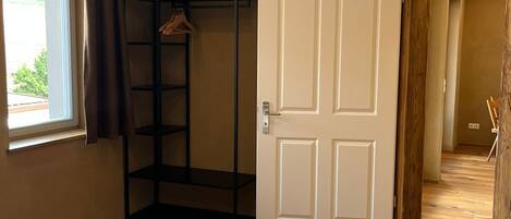 Een slaapkamer met een bed, een kledingkast, een hangplank en een deur naar een andere kamer.