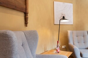 Une pièce avec un canapé gris, une table d’appoint en bois sur laquelle se trouve une lampe, et une carte accrochée au mur.