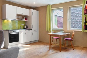 Une cuisine compacte avec des meubles blancs, un pare-feu vert et un coin repas comprenant une table et des chaises.