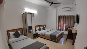 A hotel room with two beds, a desk, a mirror, and a ceiling fan. - LOKTAK RESIDENCY (Guwahati)