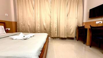 Habitación de hotel con cama, escritorio, silla, televisión y ventana con cortinas.