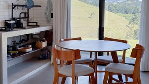 A kitchen with a dining area, a view of rolling hills, and a large window. - Loft in the Mantiqueira house. (Gonçalves)
