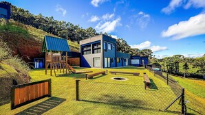 A modern building with a flat roof, large windows, and a well-maintained lawn with a playground. - Loft in the Mantiqueira house. (Gonçalves)