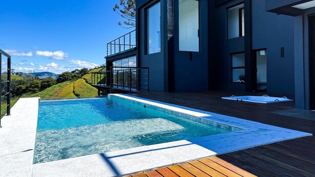 A modern house with a swimming pool, large windows, and a view of the hills. - Loft in the Mantiqueira house. (Gonçalves)