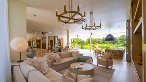 A spacious living area with a large sofa, round coffee table, and a view of a pool and garden. - Ultra-Modern 6-Bedroom in GolfCourse PH6 (Cha-am)