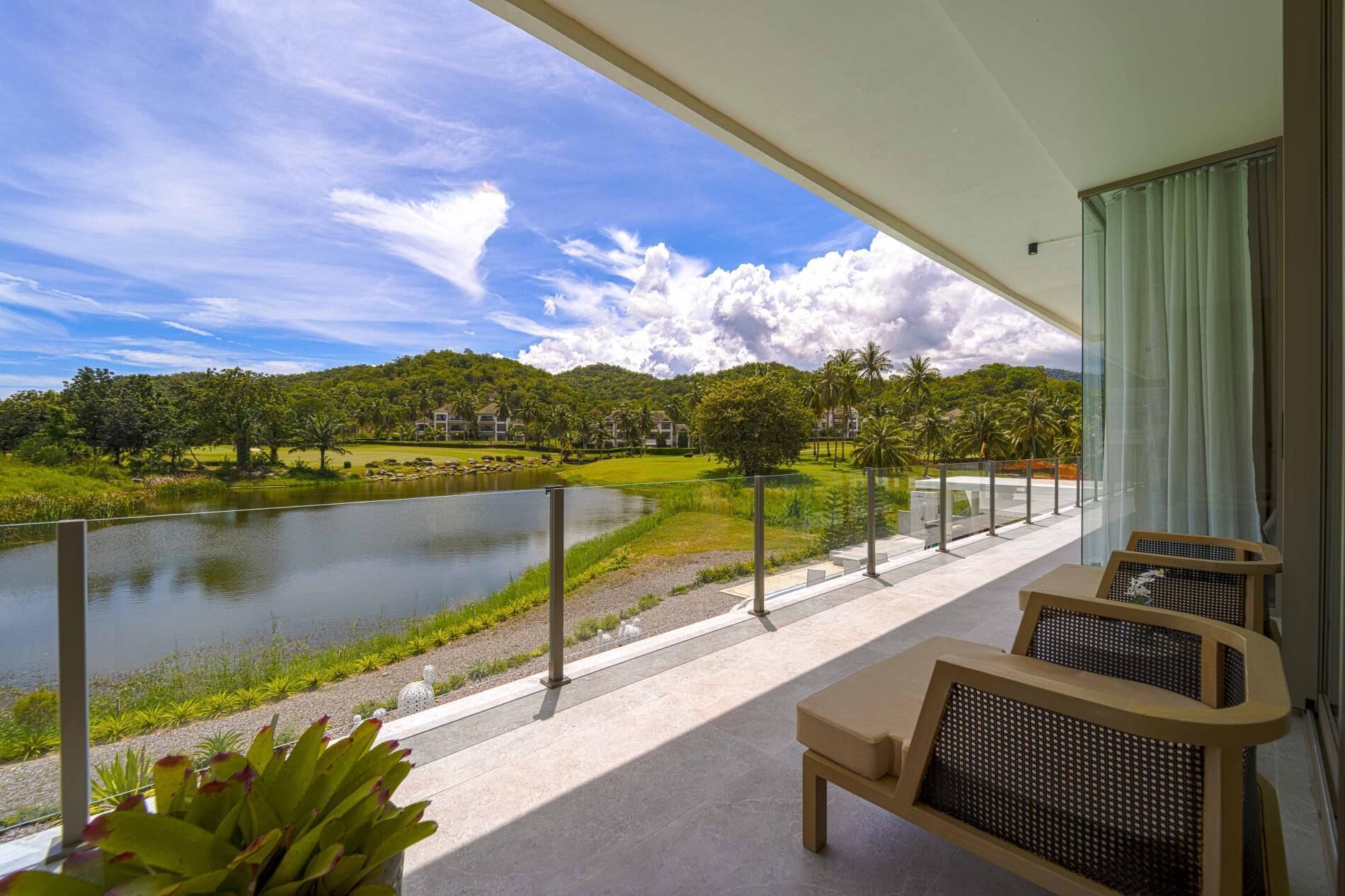A balcony with a view of a lake, greenery, and a distant building.
