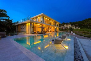 Ein modernes, zweistöckiges Haus mit Swimmingpool, Sitzgelegenheiten im Freien und einer gut beleuchteten Terrassenfläche.
