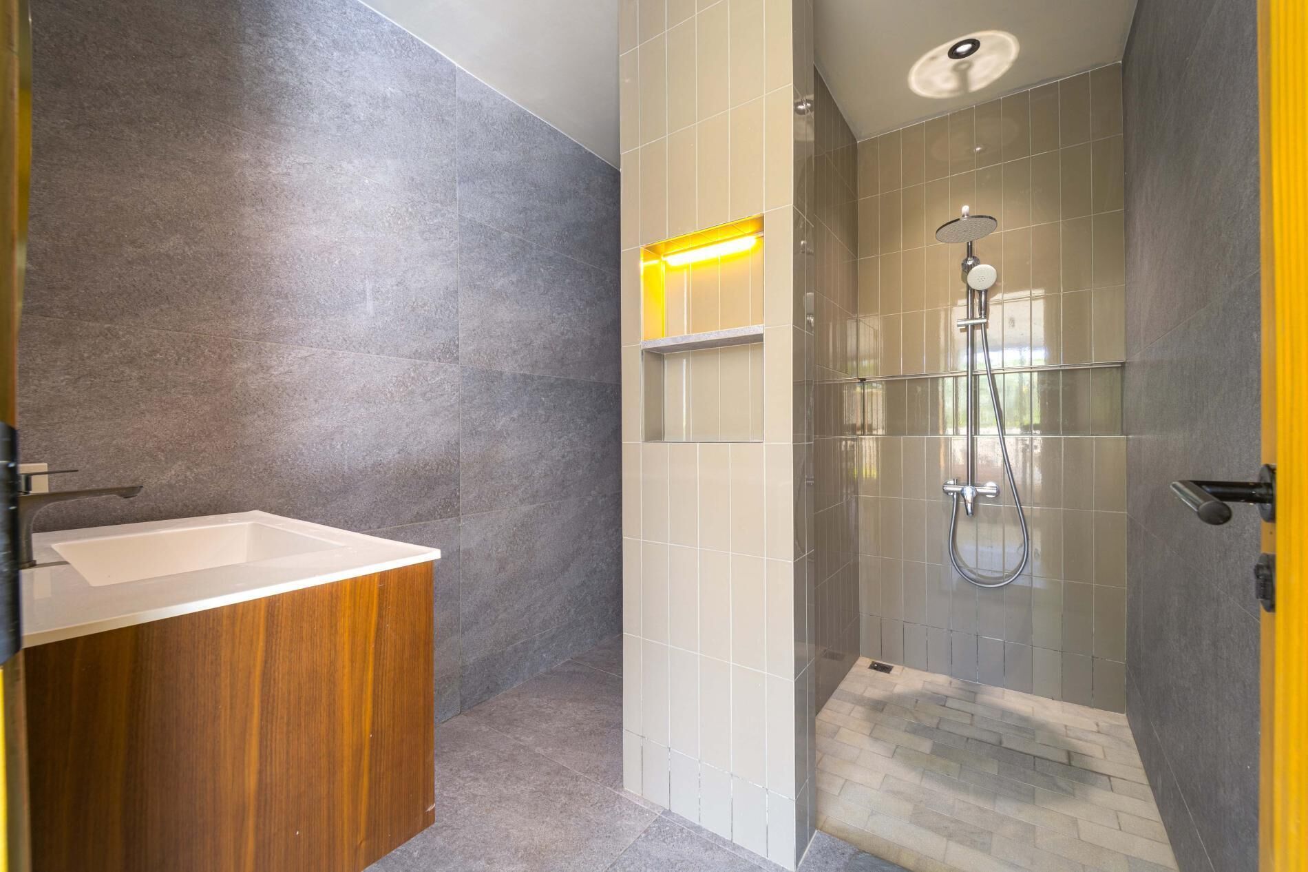 A modern bathroom with a wooden vanity, a glass shower enclosure, and a yellow accent wall.