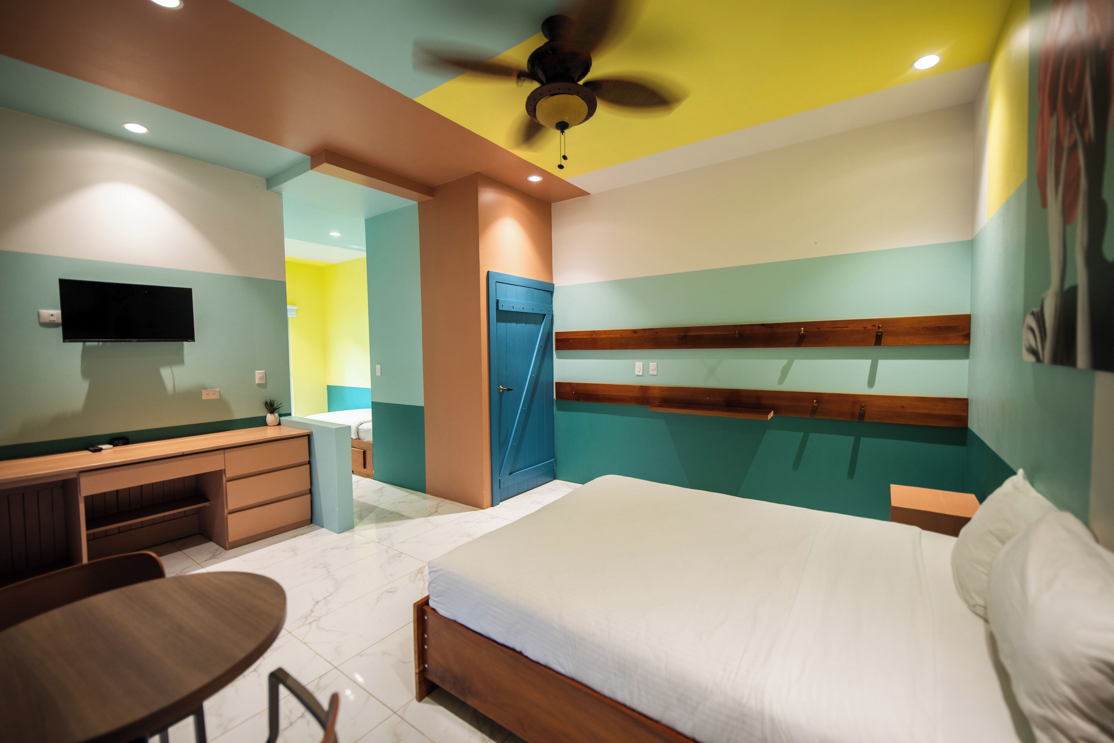 Una habitación de hotel con cama, escritorio, silla y televisor en la pared.