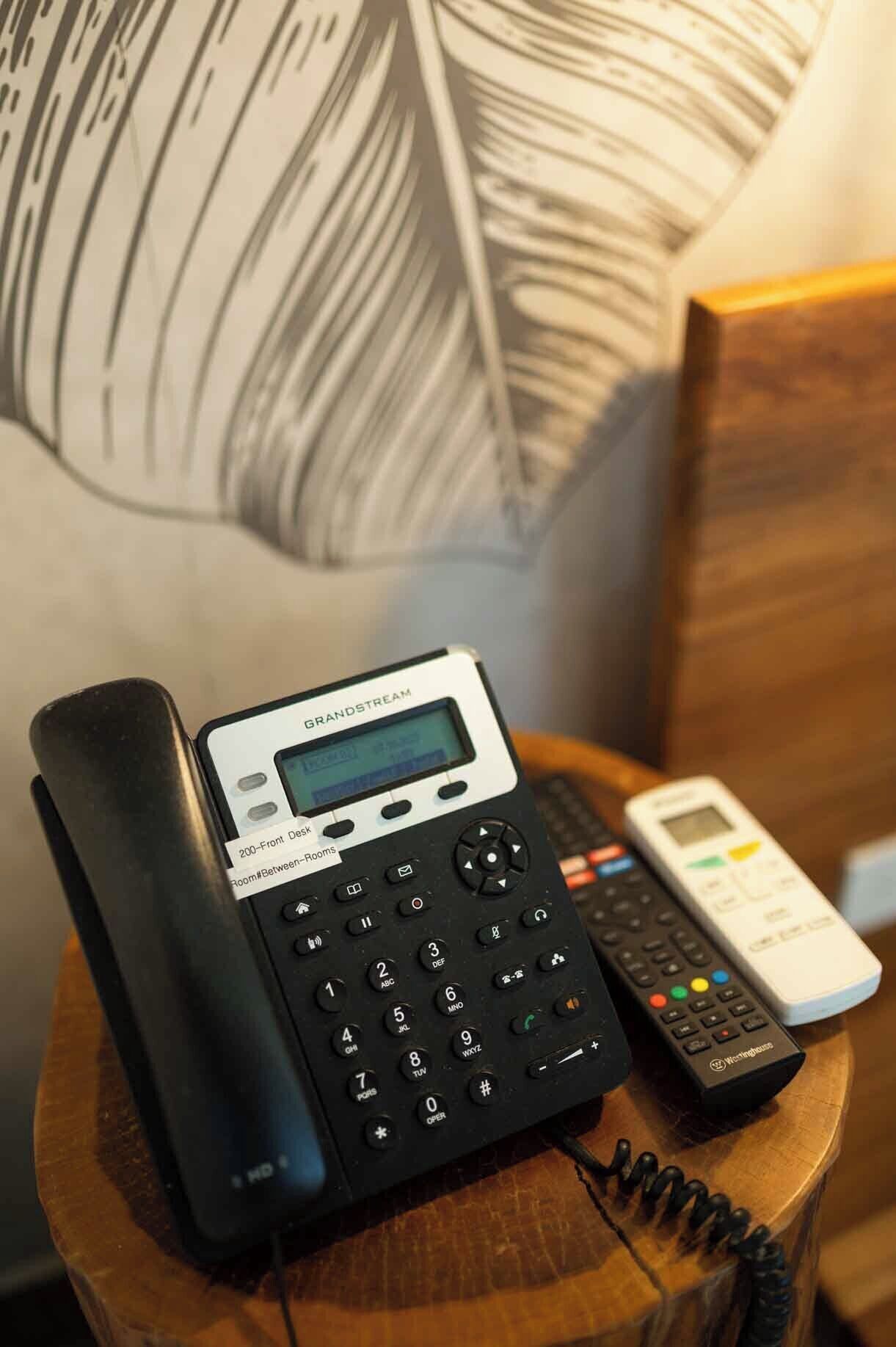 A Grandstream cordless phone on a wooden nightstand with a remote control beside it.
