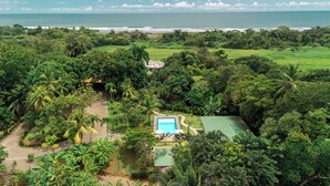 An aerial view of a tropical resort with a swimming pool, lush greenery, and a view of the ocean. - Villa Marala (Parrita)