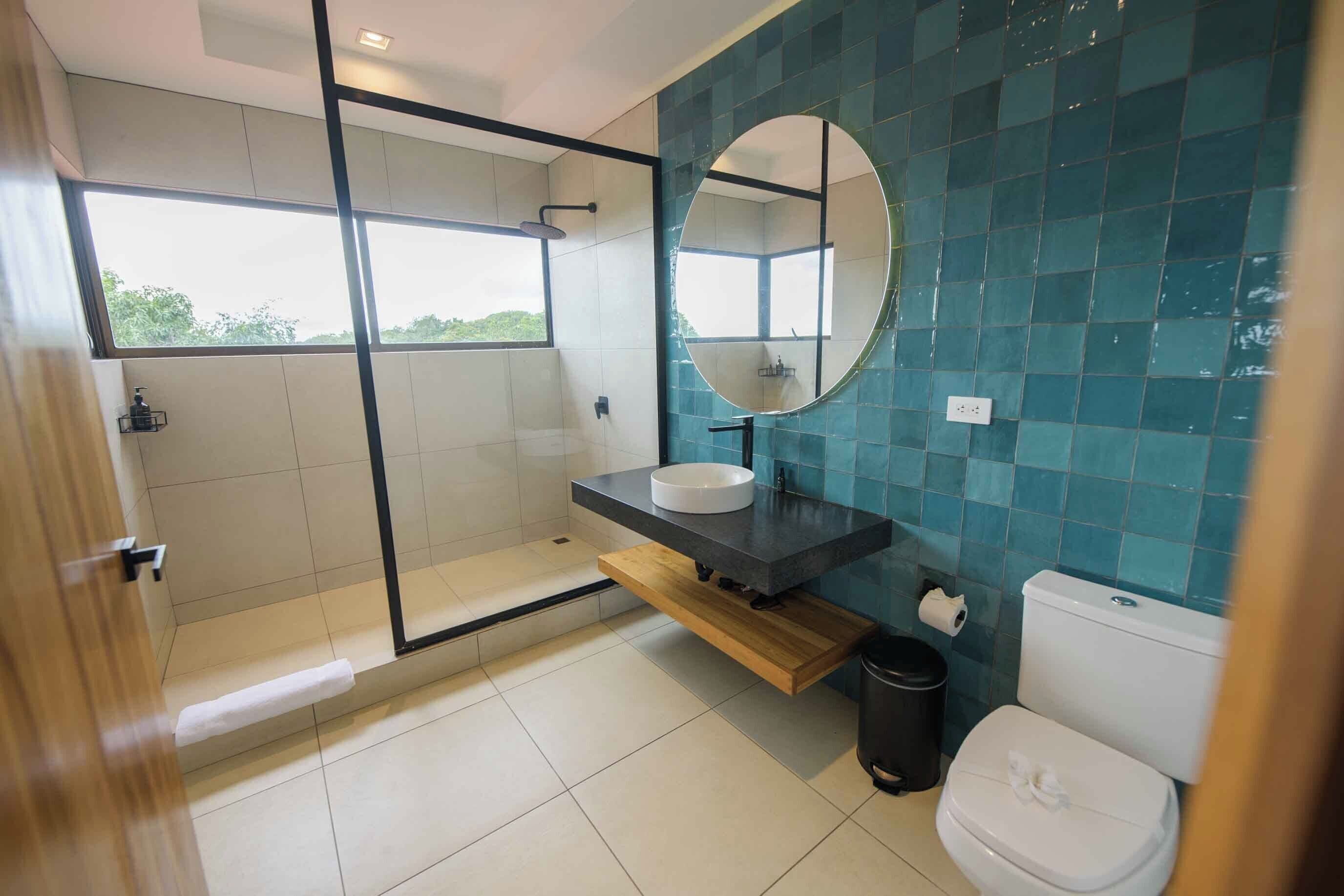 Un baño moderno con ducha de mampara de vidrio, lavamanos blanco y un inodoro.