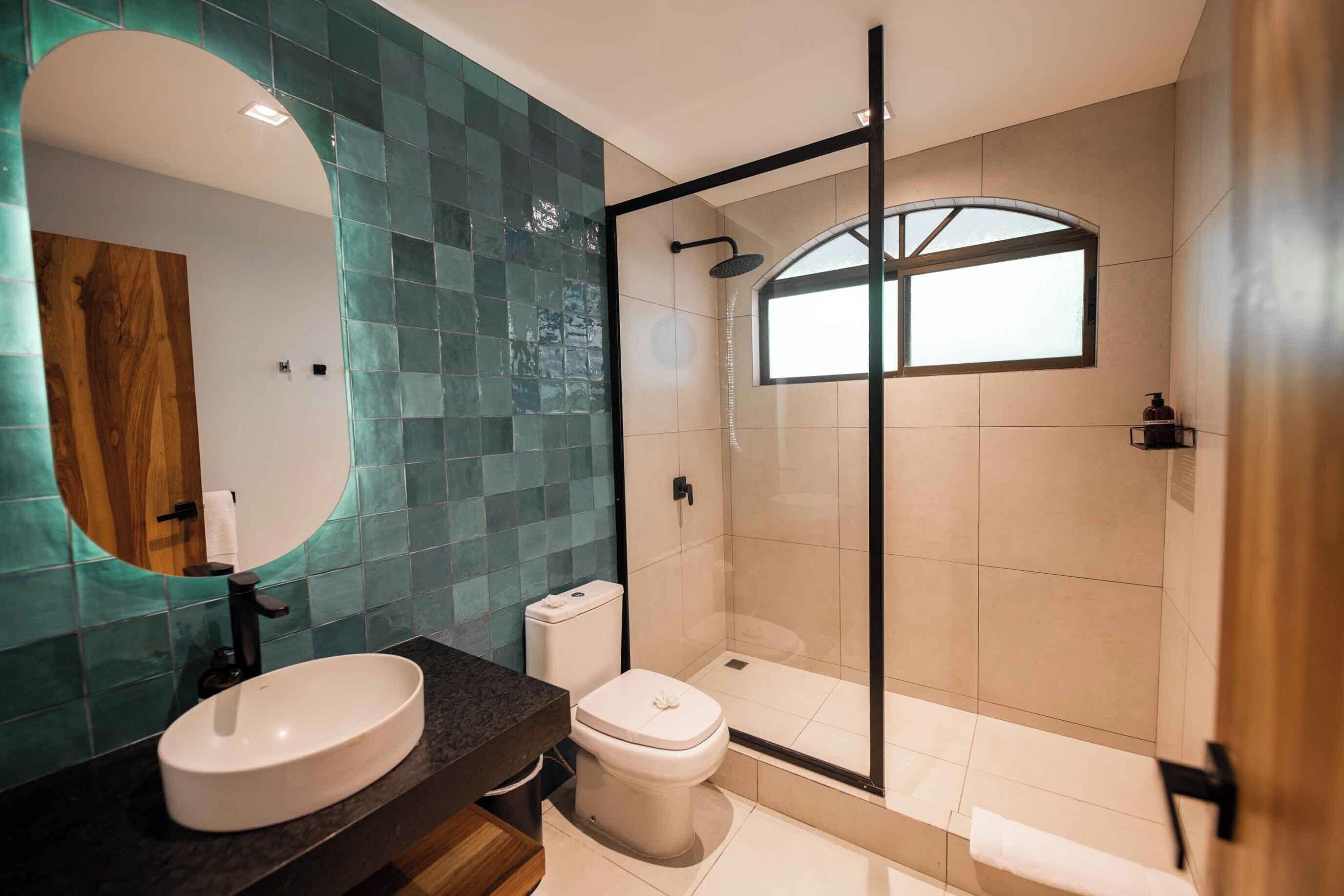 A modern bathroom with a large mirror, a sink, a toilet, and a glass-enclosed shower.