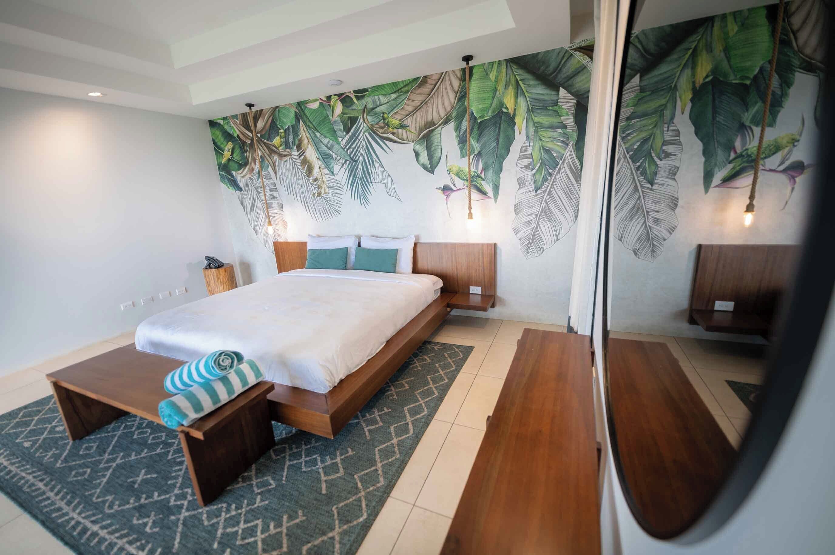 A modern bedroom with a large bed, a wooden nightstand, a small table, and a patterned rug.