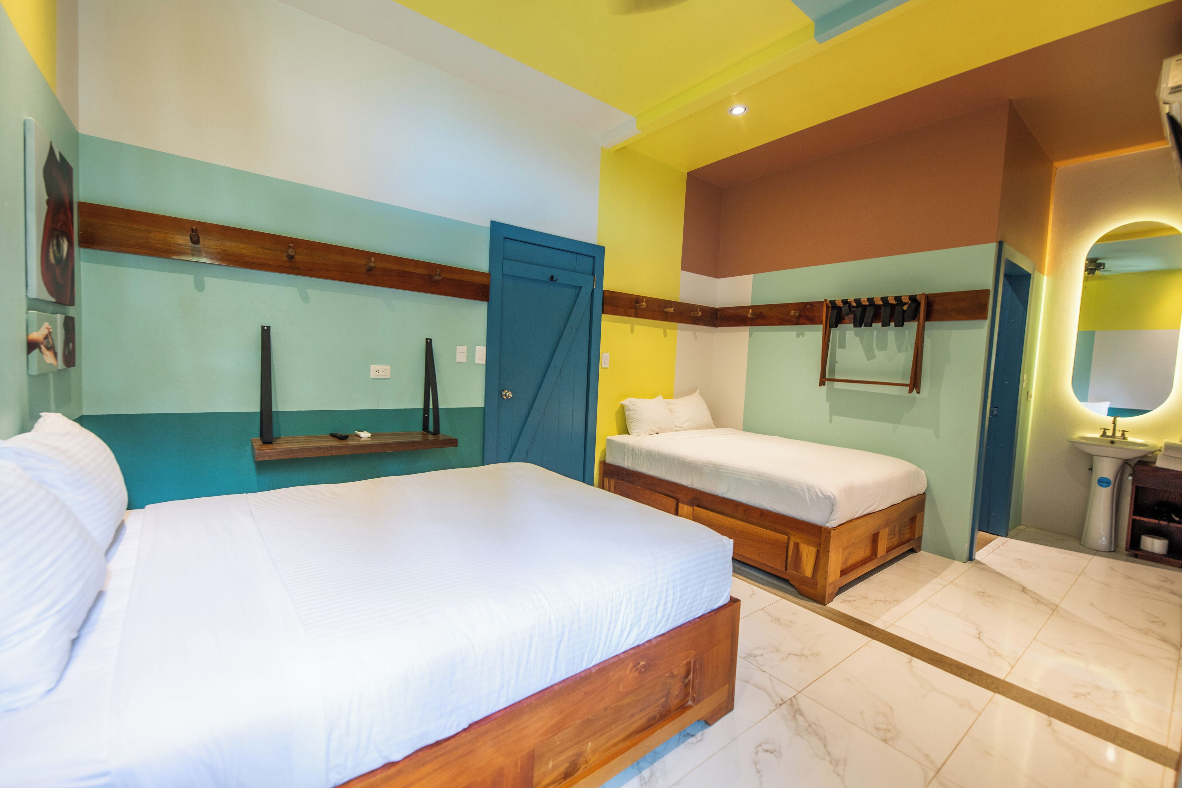 A hotel room with two beds, a wooden headboard, a mirror, and a sink.