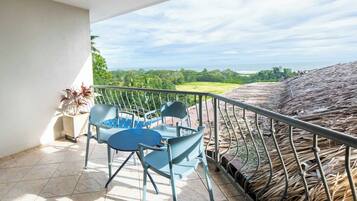 A balcony with a table and chairs, a potted plant, and a view of a lush landscape and ocean.