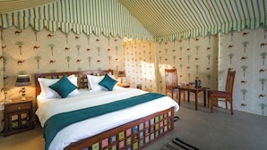 A room with a striped tent ceiling, a bed with a patterned headboard, and a wall with camel and palm tree wallpaper. - Shreeji Desert Resort (Sam)