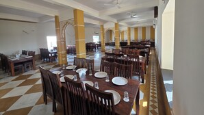 A spacious dining area with high ceilings, multiple tables set for dining, and decorative columns. - Shreeji Desert Resort (Sam)