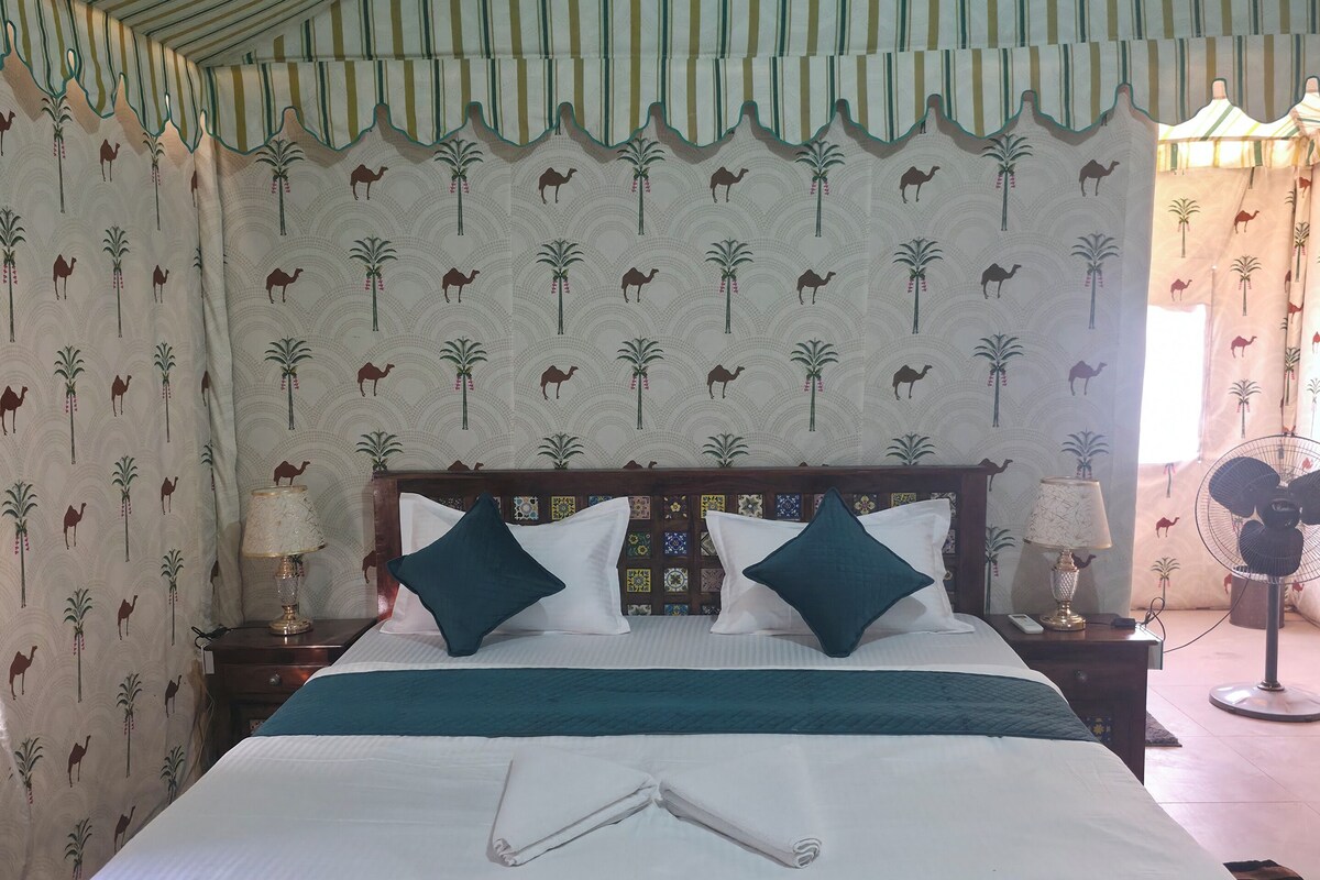 A bed with a patterned headboard, a bedside table with a lamp, and a wall with a camel and palm tree pattern.