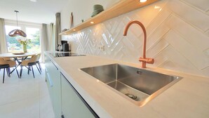 A modern kitchen with a stainless steel sink, wooden countertop, and a herringbone tile backsplash. - Modern vakantiehuis aan de kust! (Callantsoog)