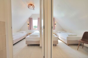 Une chambre moderne et bien éclairée, équipée de deux lits simples, d’une petite table et d’une chaise.