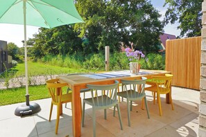 Un espace extérieur aménagé pour les repas, avec une table et des chaises en bois, un parasol vert et une vue sur le jardin.