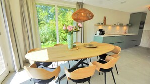 A modern kitchen with a dining area, featuring a round wooden table, matching chairs, and a hanging light fixture. - Modern vakantiehuis aan de kust! (Callantsoog)