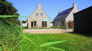 A modern house with a sloped roof, a patio with a table and chairs, and a garden area. - Modern vakantiehuis aan de kust! (Callantsoog)