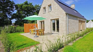 A modern house with a sloped roof, a brick exterior, and a patio with a table and chairs under a green umbrella. - Modern vakantiehuis aan de kust! (Callantsoog)