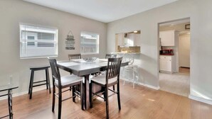 A dining area with a wooden table and chairs, a chandelier, and a view into the kitchen. - Family Pet Friendly Getaway With Porch Fire Pit Yard (Tampa)