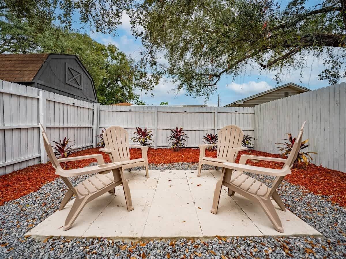 Une terrasse avec deux chaises beiges et une table blanche, entourée d’une clôture blanche et d’un paillis rouge.