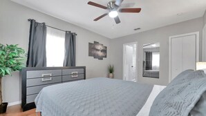A bedroom with a bed, a ceiling fan, a dresser, a potted plant, and a door leading to another room. - Family Pet Friendly Getaway With Porch Fire Pit Yard (Tampa)