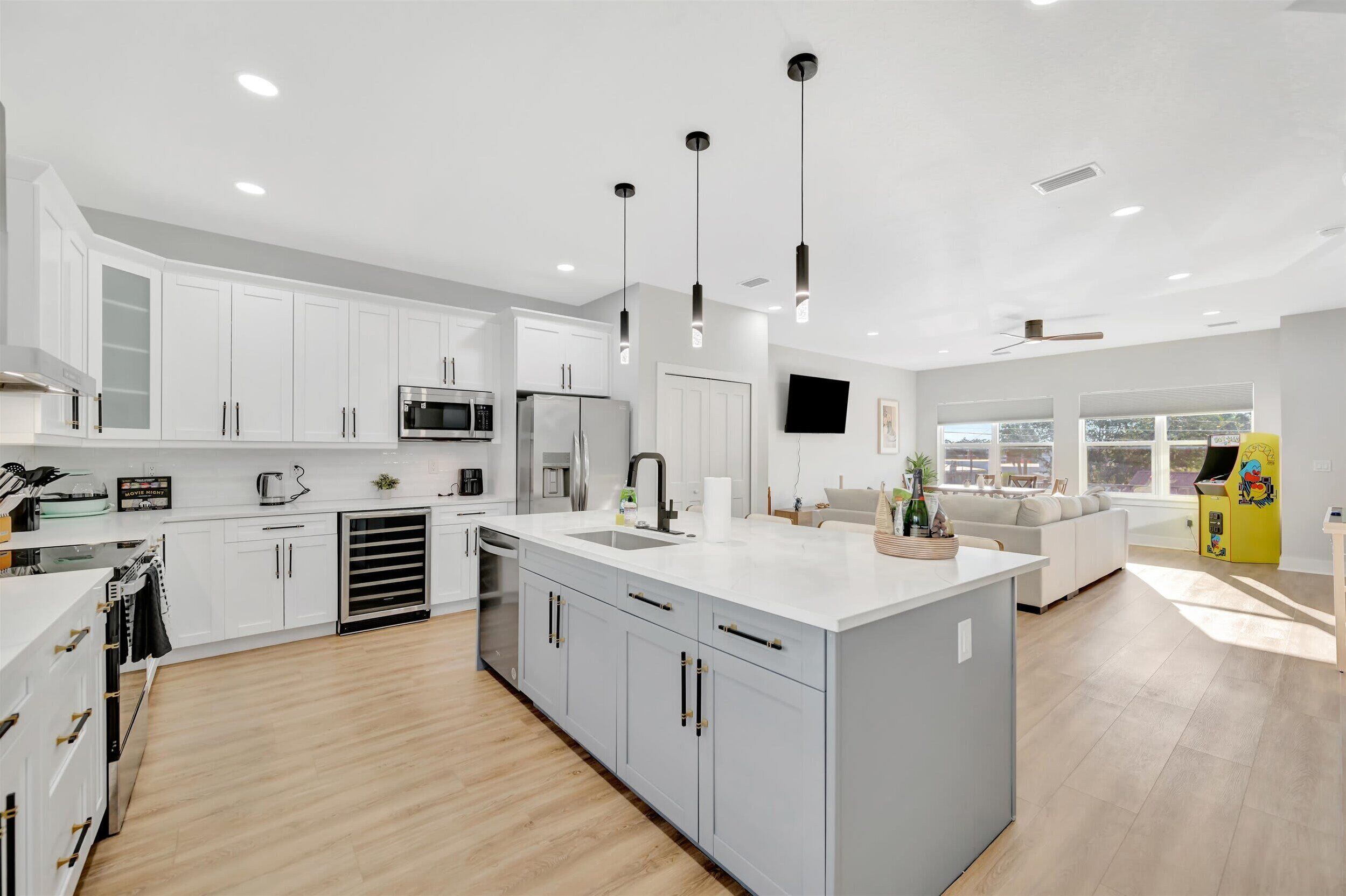 Una cocina moderna con armarios blancos, una isla central y un comedor con sofá y un mueble amarillo.