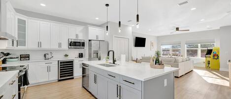 Una cocina moderna con armarios blancos, una isla central y un comedor con sofá y un mueble amarillo.