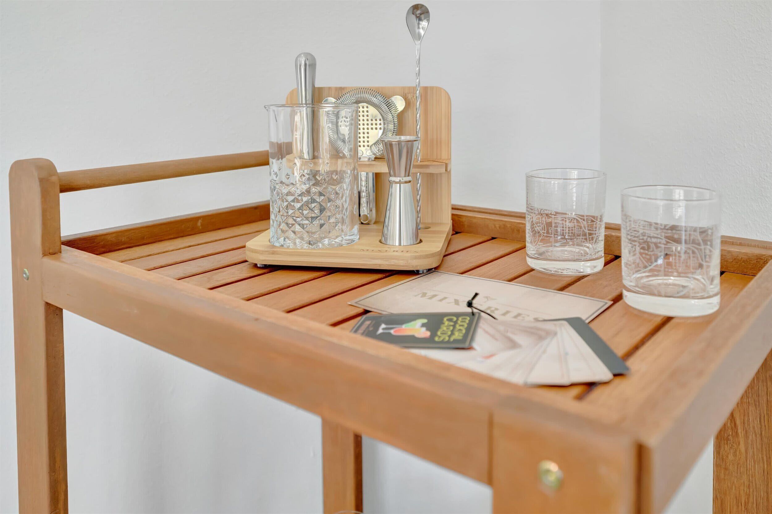 Una bandeja de madera con un rallador, dos vasos y una revista sobre una pared blanca.
