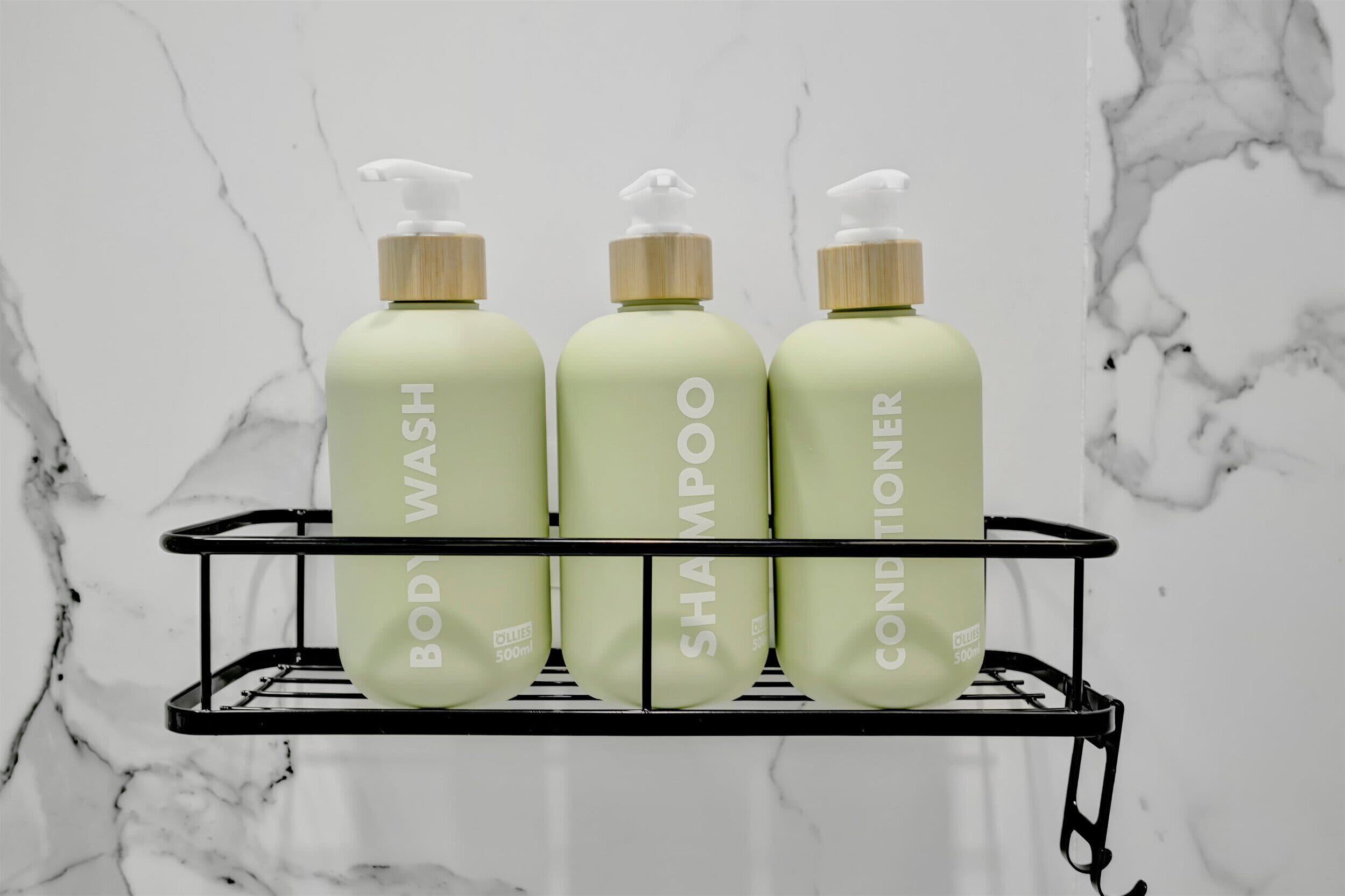Three bottles of body wash, shampoo, and conditioner on a black metal shelf against a white marble wall.