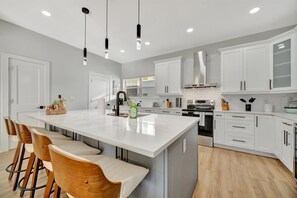 A modern kitchen with white cabinets, a large island with bar stools, and pendant lighting. - 4br3ba Modern Sleeps 10 8 Minutes to Raymond James (Tampa)