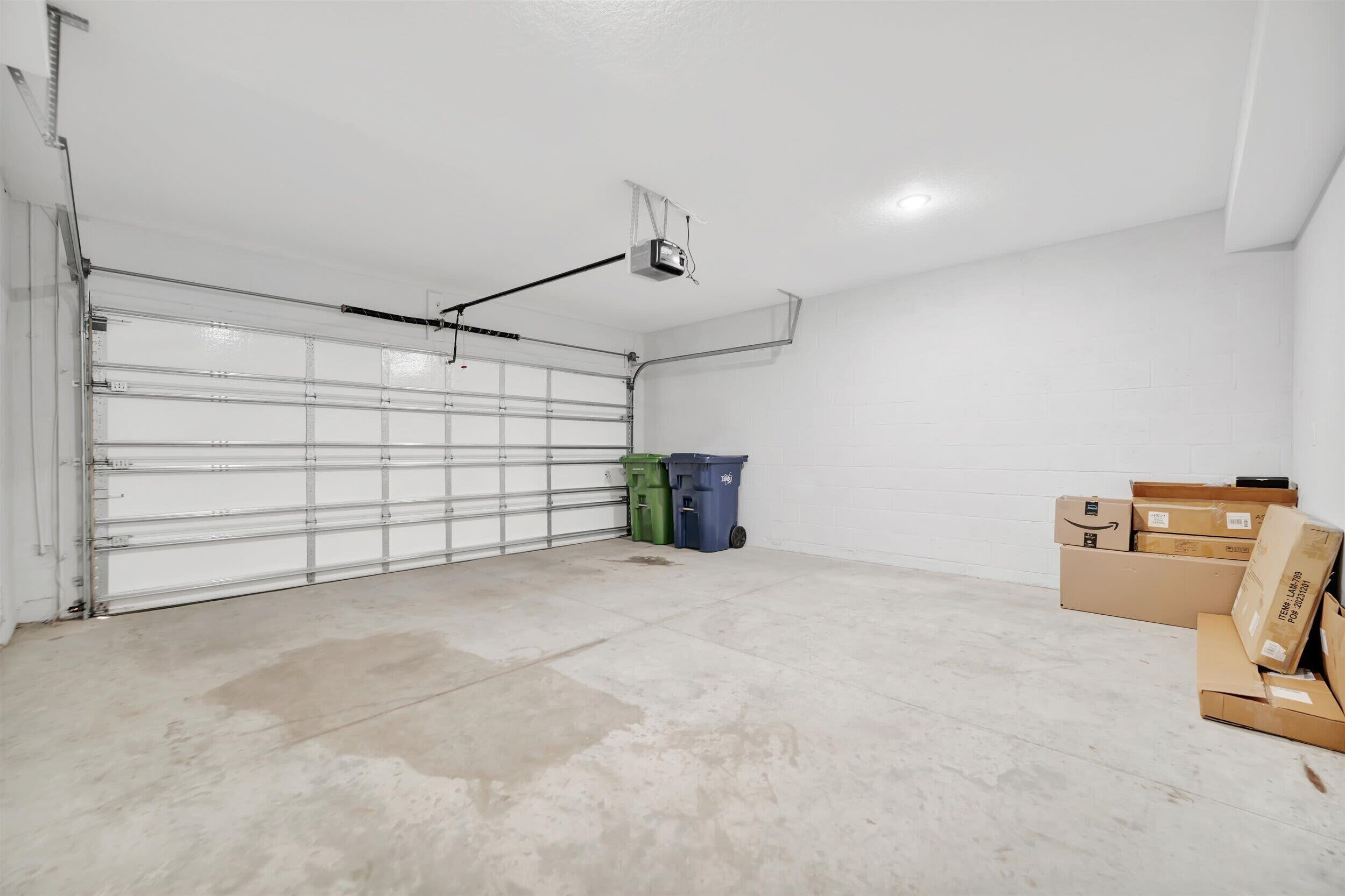 A garage with a closed garage door, a projector mounted on the ceiling, and several cardboard boxes and trash bins on the floor.
