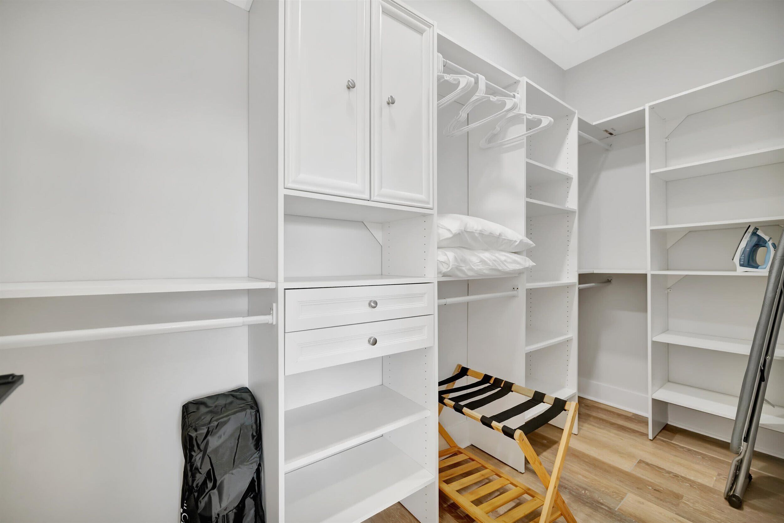 A white closet with open shelves, a wooden drying rack, and hanging clothes.