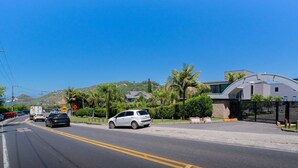 A street with cars, a white car parked on the side, and a modern building with a curved roof. - Studio 290 m From Praia Mole Vds0005 (Florianópolis)