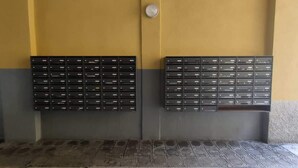 Due file di cassette postali nere fissate a una parete, con una combinazione di colori giallo e grigio.
