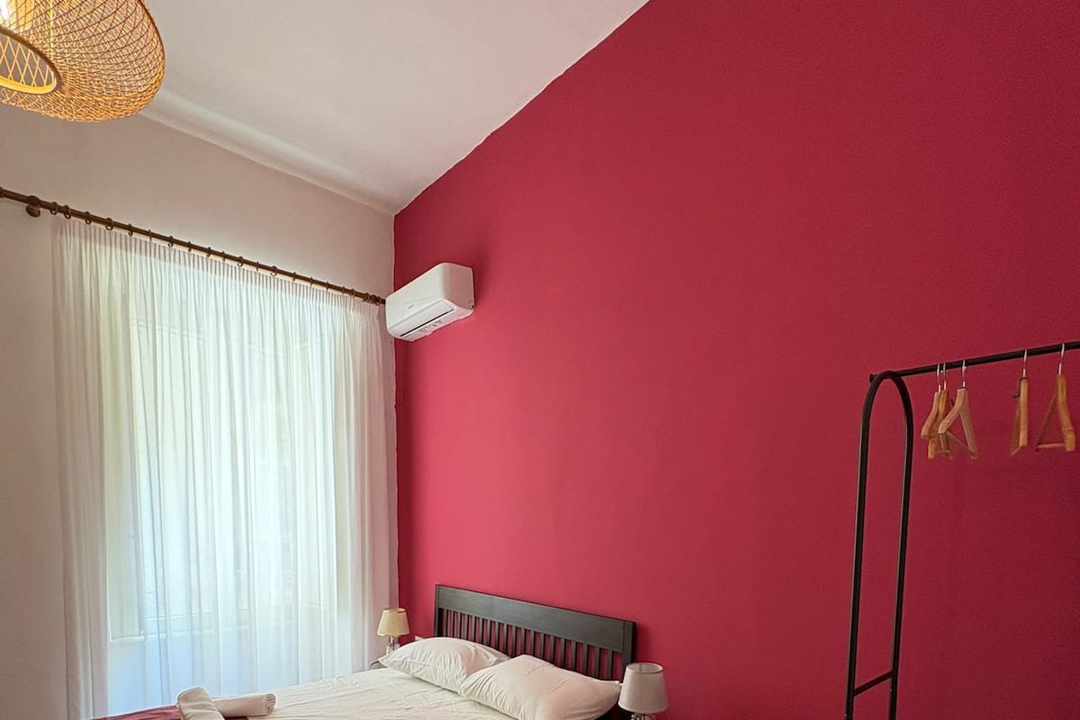 A bedroom with a bed, a bedside table, a hanging light fixture, a radiator, and a wardrobe.